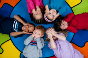 Six preschool children lay in a circle on a colorful background